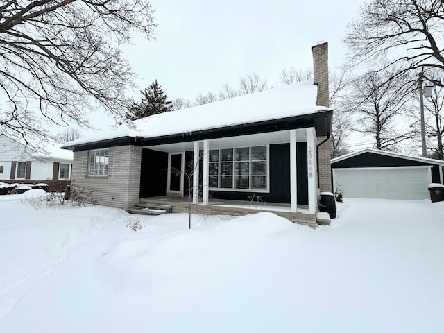 snow covered back of property featuring an outbuilding and a garage