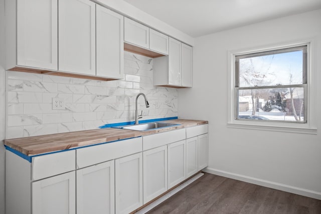 kitchen with butcher block countertops, decorative backsplash, dark hardwood / wood-style flooring, sink, and white cabinetry