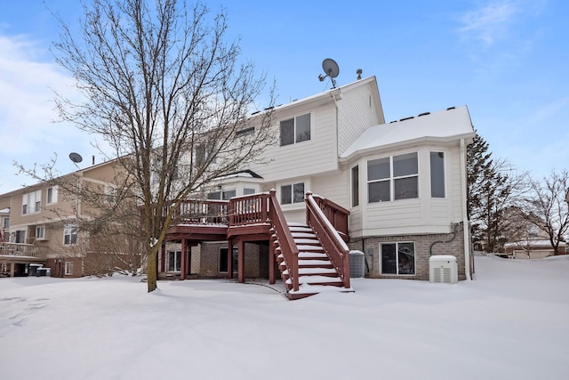 snow covered property featuring a deck, brick siding, and stairway