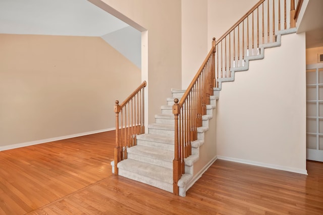 staircase featuring high vaulted ceiling, baseboards, and wood finished floors