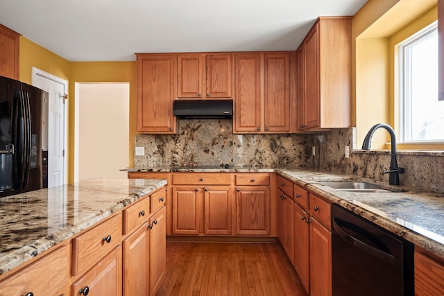 kitchen with light stone counters, light wood-style floors, a sink, under cabinet range hood, and black appliances