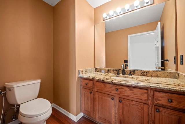 half bath featuring baseboards, vanity, toilet, and wood finished floors