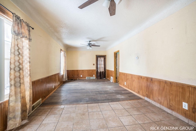 tiled empty room with ceiling fan, wooden walls, and a textured ceiling