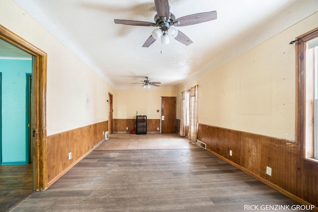 unfurnished room featuring ceiling fan, hardwood / wood-style flooring, wooden walls, and a textured ceiling