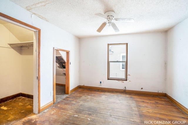 unfurnished bedroom featuring a walk in closet, dark wood-type flooring, a textured ceiling, and a closet