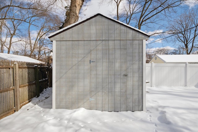 snow covered structure with an outbuilding, a shed, and a fenced backyard