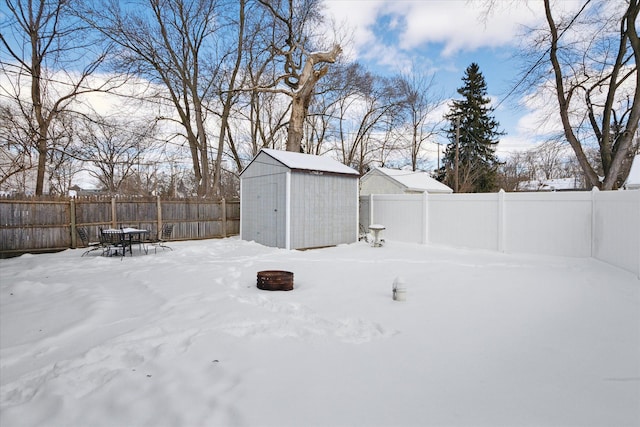 yard covered in snow featuring a fenced backyard, a storage unit, and an outbuilding