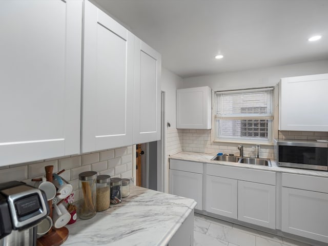 kitchen with tasteful backsplash, sink, white cabinets, and light stone counters