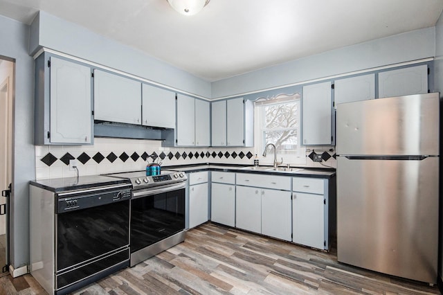 kitchen featuring range hood, sink, backsplash, stainless steel appliances, and light wood-type flooring