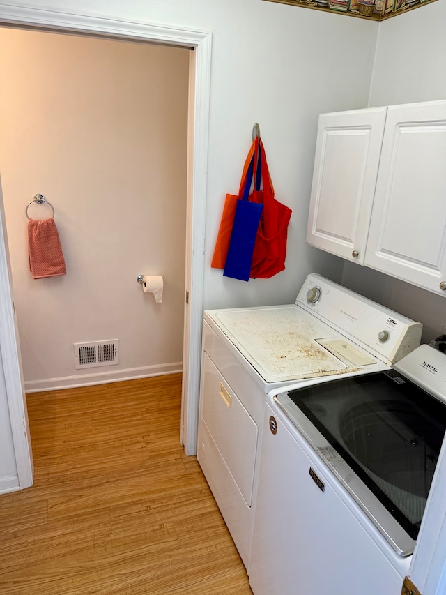 laundry area with light hardwood / wood-style flooring, washer and clothes dryer, and cabinets