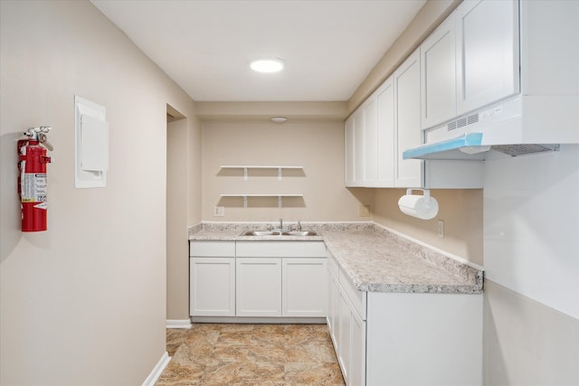 kitchen featuring light countertops, white cabinets, a sink, under cabinet range hood, and baseboards