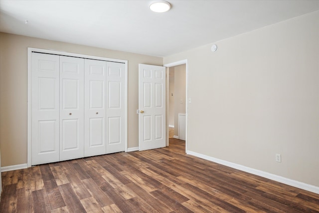 unfurnished bedroom with a closet, baseboards, and dark wood-style flooring