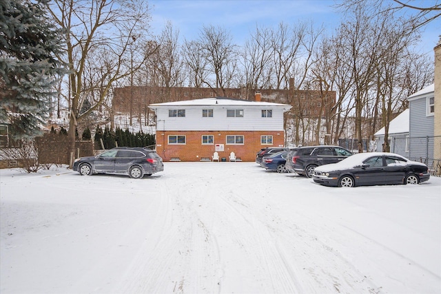 snow covered parking area featuring uncovered parking and fence