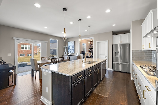 kitchen with a center island with sink, stainless steel appliances, sink, white cabinets, and pendant lighting