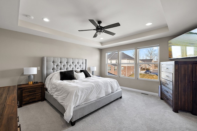 bedroom with ceiling fan, a tray ceiling, and light colored carpet