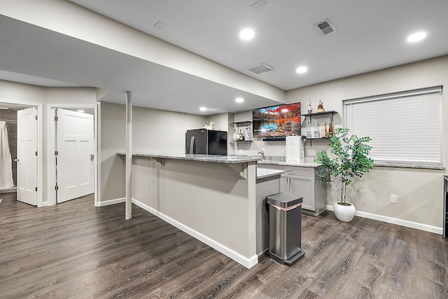 kitchen with a breakfast bar area, dark hardwood / wood-style flooring, kitchen peninsula, and black fridge with ice dispenser