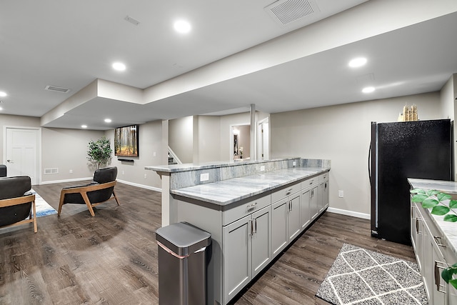 kitchen featuring dark wood-type flooring, black refrigerator, a kitchen bar, and light stone countertops