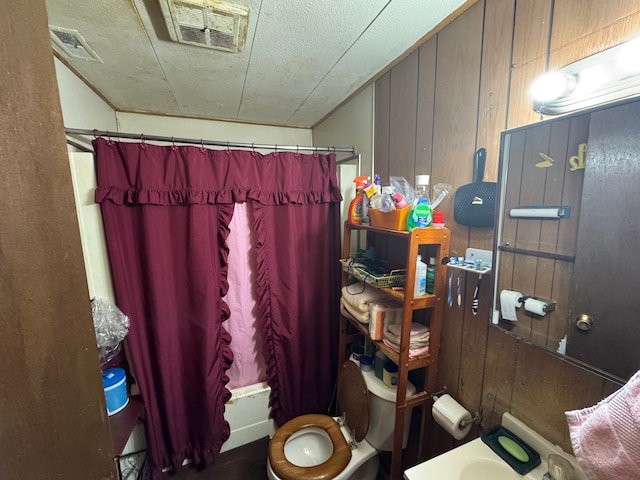 bathroom with a shower with curtain, wood walls, a textured ceiling, and toilet