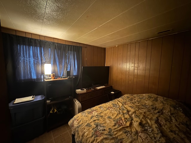 bedroom featuring tile patterned floors, a textured ceiling, and wood walls