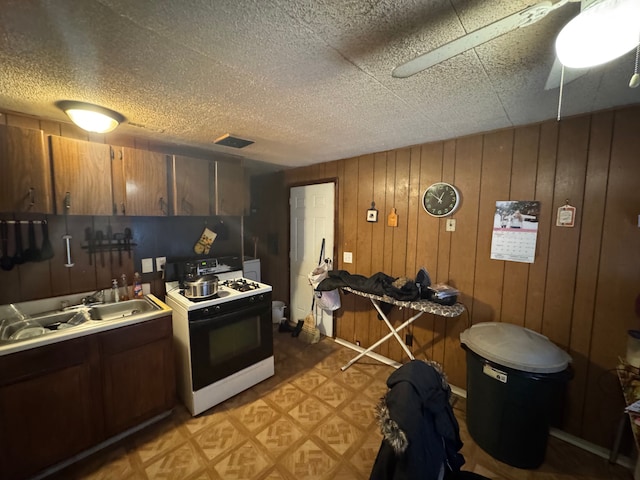 kitchen featuring range, sink, a textured ceiling, and wood walls