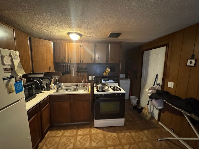 kitchen featuring range with gas stovetop, washer / dryer, sink, white refrigerator, and a textured ceiling