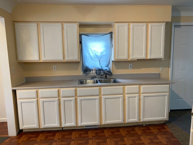 kitchen with sink, white cabinetry, and dark parquet flooring