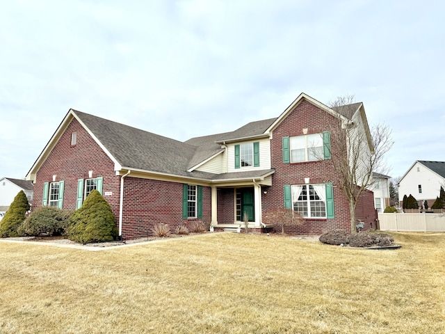 view of front of property with a front yard, fence, brick siding, and roof with shingles