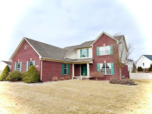 view of front facade with brick siding, a shingled roof, a front lawn, and fence