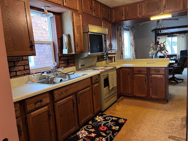 kitchen featuring white range with gas cooktop, brown cabinets, a peninsula, light countertops, and a sink