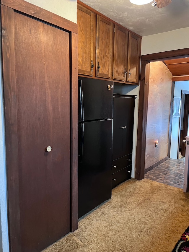 kitchen featuring brown cabinetry, freestanding refrigerator, and light colored carpet