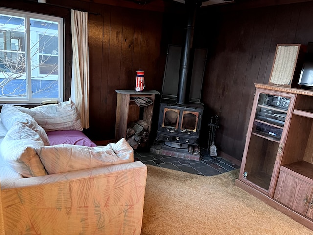 carpeted living area with a wood stove and wood walls