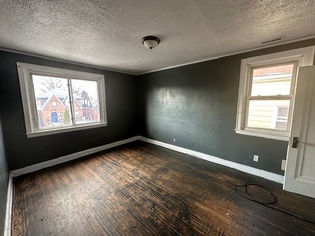 spare room featuring dark wood-type flooring, a healthy amount of sunlight, and a textured ceiling