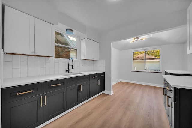 kitchen with tasteful backsplash, sink, white cabinets, and light wood-type flooring