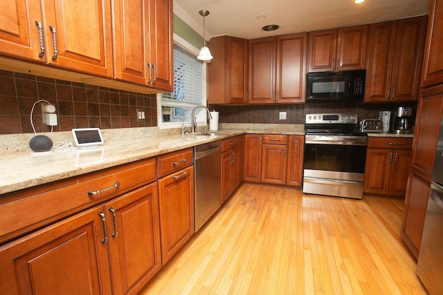 kitchen with a sink, hanging light fixtures, appliances with stainless steel finishes, light wood-type flooring, and light stone countertops