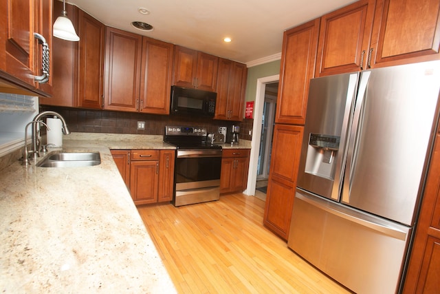 kitchen featuring hanging light fixtures, a sink, stainless steel appliances, light wood-type flooring, and backsplash