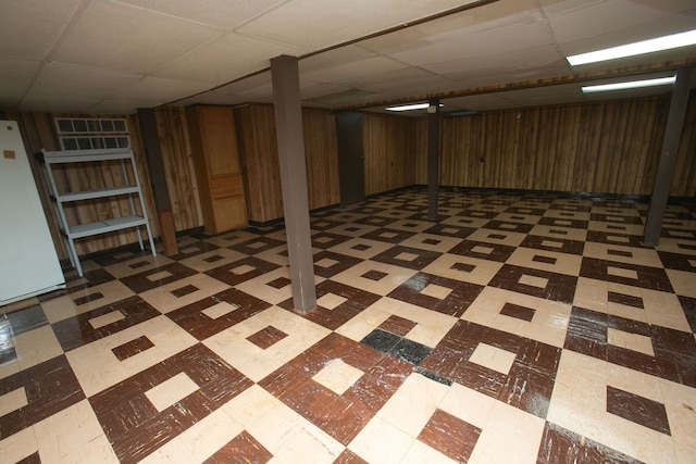 finished below grade area featuring a drop ceiling, freestanding refrigerator, and tile patterned floors