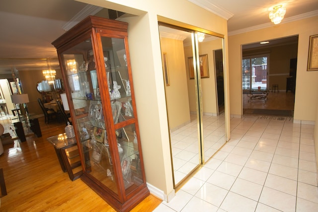 hall with light tile patterned floors, ornamental molding, baseboards, and a notable chandelier