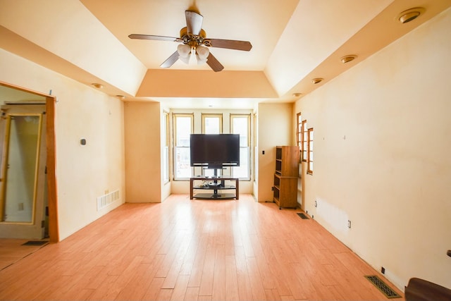 unfurnished living room with ceiling fan, a raised ceiling, and light wood-type flooring