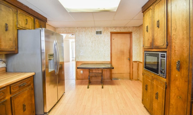 kitchen featuring black microwave, stainless steel refrigerator with ice dispenser, a drop ceiling, and light hardwood / wood-style flooring