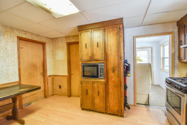 kitchen featuring black microwave, stainless steel gas range oven, a paneled ceiling, and light hardwood / wood-style flooring