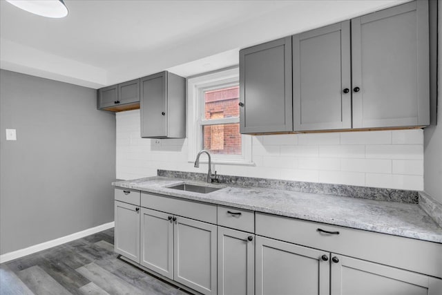 kitchen featuring sink, gray cabinetry, tasteful backsplash, hardwood / wood-style flooring, and light stone countertops