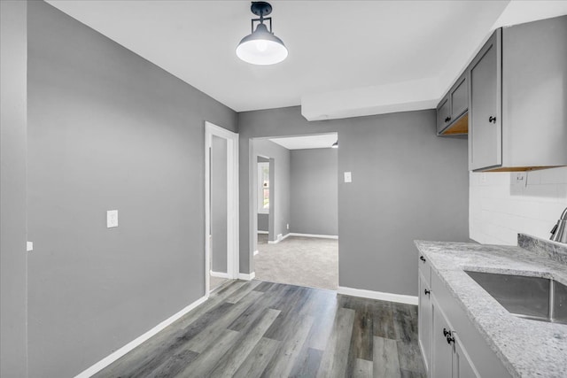 kitchen with pendant lighting, sink, gray cabinets, hardwood / wood-style floors, and light stone countertops