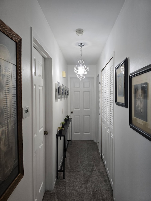 hall featuring an inviting chandelier and dark colored carpet