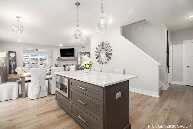 kitchen with a kitchen island, stainless steel microwave, light hardwood / wood-style floors, and decorative light fixtures