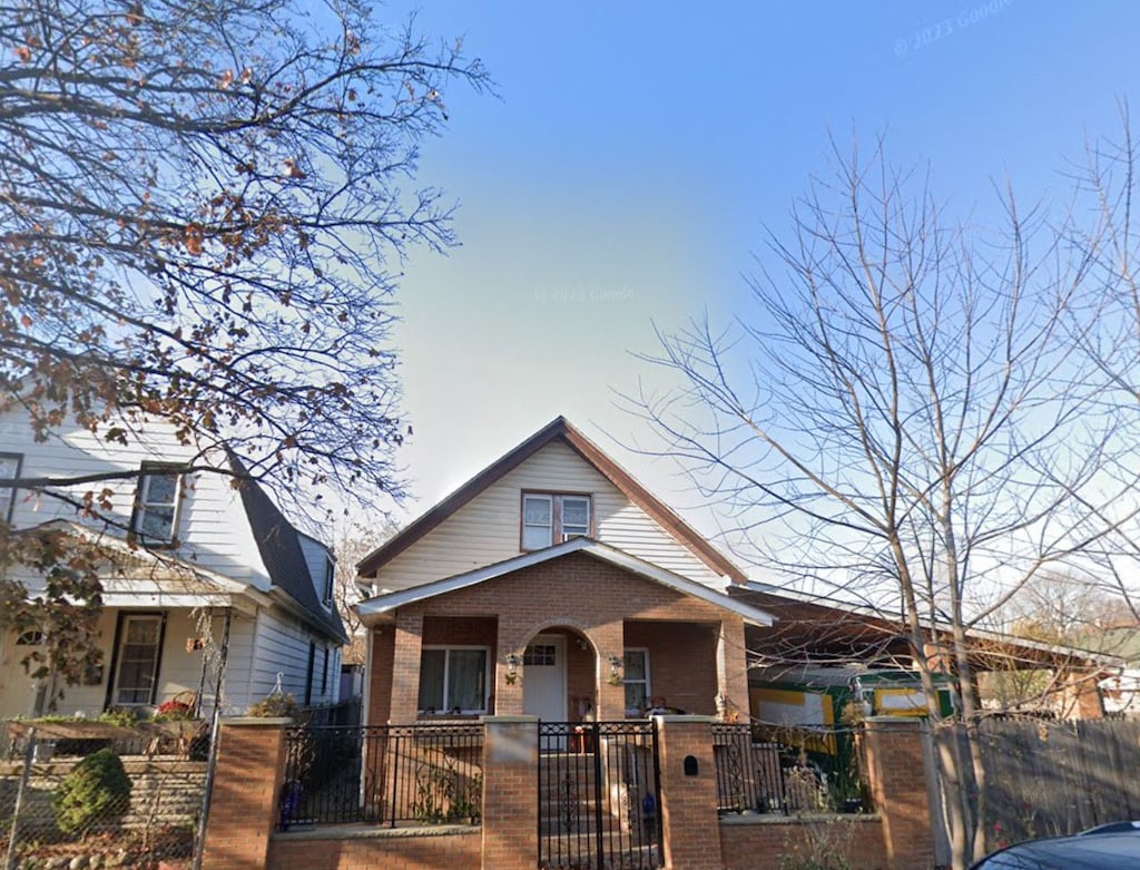 bungalow-style home featuring covered porch, brick siding, a fenced front yard, and a gate