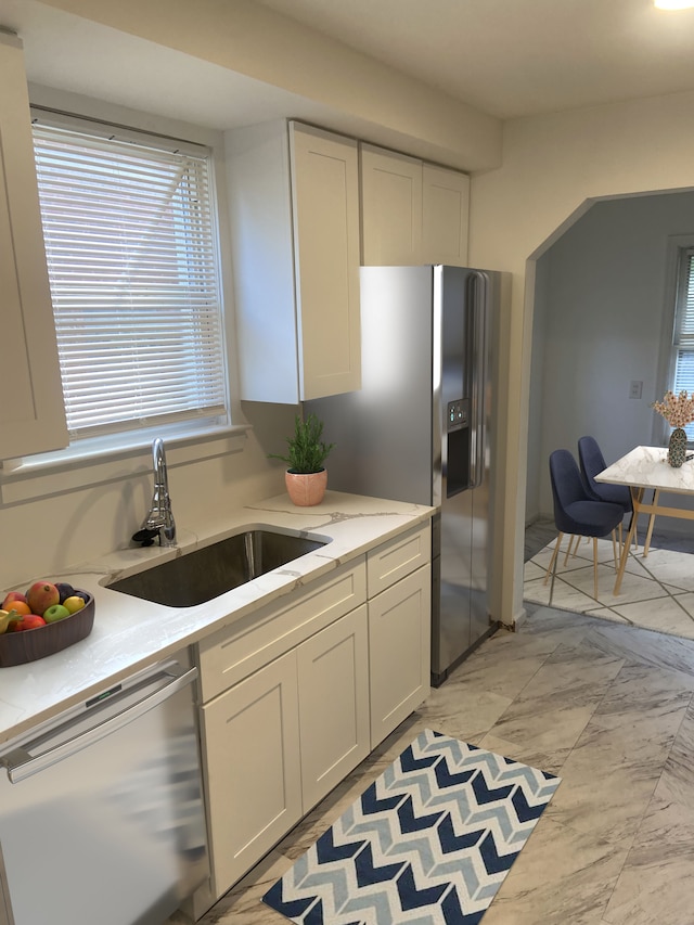 kitchen featuring arched walkways, stainless steel appliances, light countertops, white cabinetry, and a sink