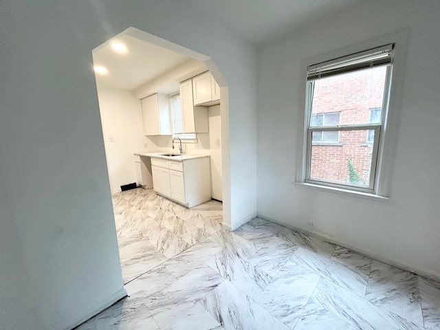 kitchen with arched walkways, marble finish floor, light countertops, white cabinetry, and a sink