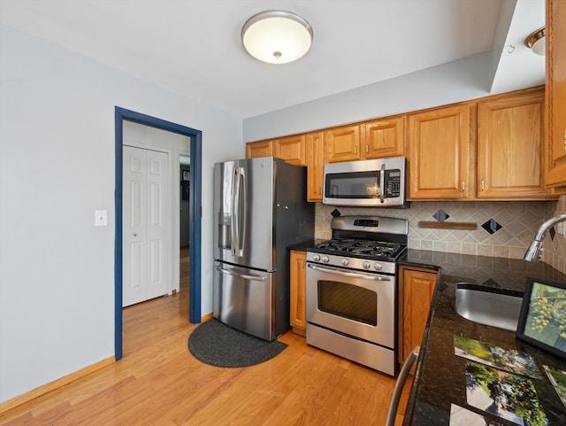 kitchen featuring dark stone countertops, light hardwood / wood-style flooring, sink, backsplash, and stainless steel appliances