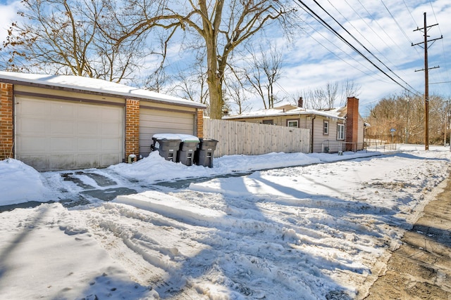 snowy yard with a garage, fence, and an outbuilding