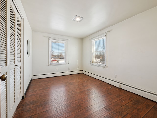 unfurnished bedroom featuring a baseboard heating unit, a closet, and dark hardwood / wood-style flooring